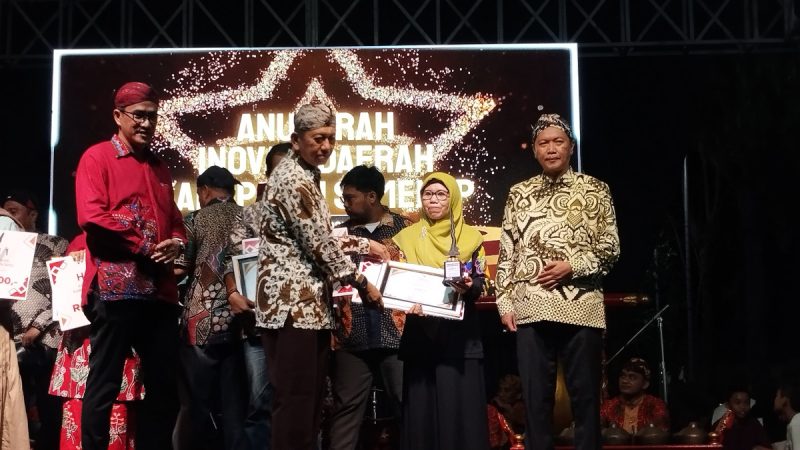 Kepala Bidang Pelayanan Pendaftaran Penduduk Disdukcapil Sumenep, Wahasah, saat menerima penghargaan inovasi daerah yang diberikan oleh Plt Sekda R. Achmad Syahwan Effendy (Za - garudajatim.com)